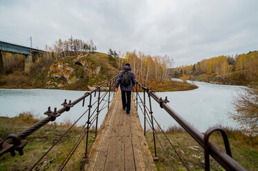 Rückansicht eines jungen männlichen Wanderers, der über einen Flusssteg geht, Kislokan, Evenk, Russland - CUF44453