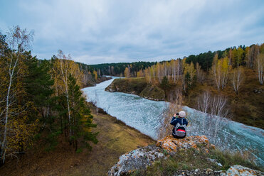 Blick von hinten auf eine junge Wanderin, die den Fluss von den Felsen aus fotografiert, Kislokan, Ewenk, Russland - CUF44454