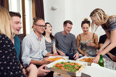 Eine Gruppe von Freunden unterhält sich bei Getränken und Pizza zu Hause - CUF44540