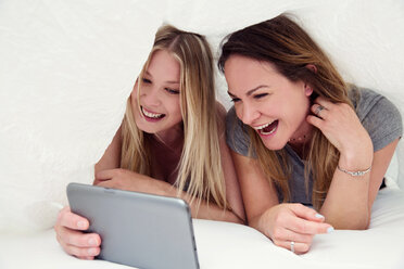 Friends underneath bed sheet using digital tablet smiling - CUF44546