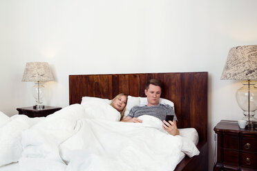 Paar liegt im Bett und benutzt ein Mobiltelefon - CUF44548