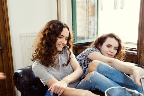 Zwei junge Freundinnen sitzen auf einem Sessel, lizenzfreies Stockfoto