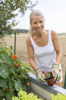 Porträt einer lächelnden Frau bei der Gartenarbeit im Hochbeet - JUNF01462