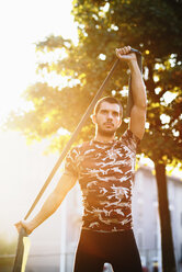 Young man exercising outdoors, using resistance band - CUF44740