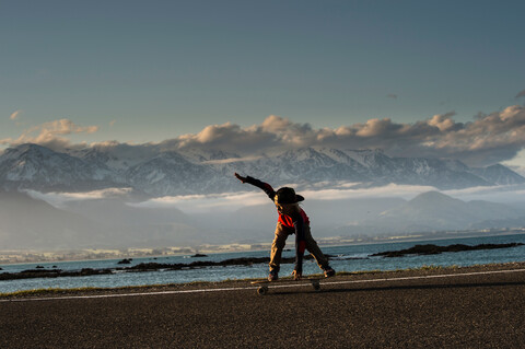 Junger Junge auf dem Skateboard entlang der Küstenstraße, Kaikoura, Gisborne, Neuseeland, lizenzfreies Stockfoto
