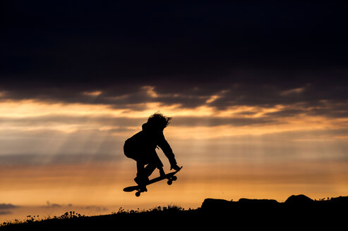 Junge fährt bei Sonnenuntergang Skateboard, springt, in der Luft, Doolin, Clare, Irland - CUF44887