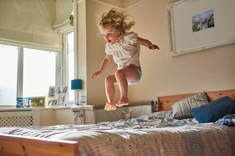 Weibliches Kleinkind springt mitten in der Luft auf dem Bett, lizenzfreies Stockfoto