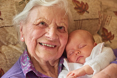 Senior woman cradling baby great granddaughter on armchair, portrait - CUF44920