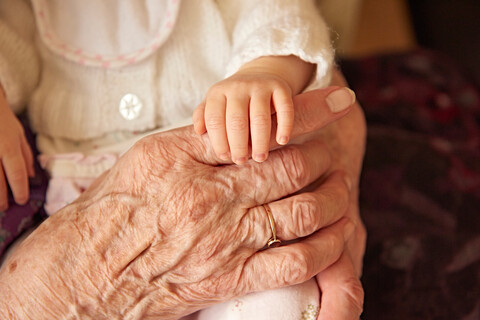 Ältere Frau hält Baby-Ur-Enkelin, Nahaufnahme der Hände, lizenzfreies Stockfoto