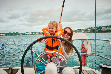 Woman steering yacht with toddler daughter, portrait, Devon, UK - CUF44922