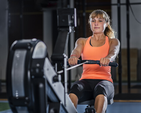 Sportliche junge Frau beim Training mit dem Rudergerät im Fitnessstudio, lizenzfreies Stockfoto