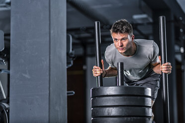 Athletic young man exercising with weight sled at gym - STSF01755