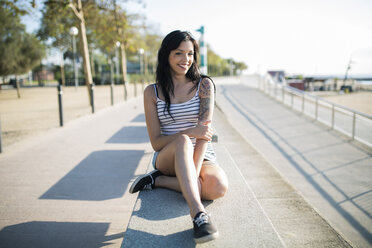 Smiling tattooed young woman relaxing on bench - GIOF04604