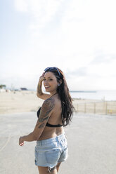 Porträt einer lächelnden jungen Frau mit Nasenpiercing und Tattoos auf dem Weg zum Strand - GIOF04618