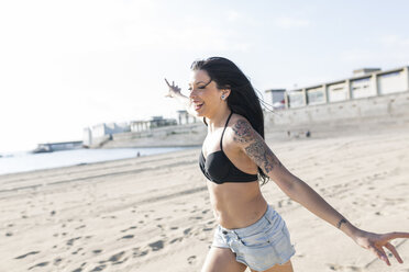 Happy young woman with tattoo running on the beach - GIOF04625