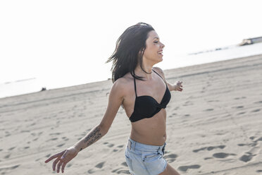 Happy young woman with tattoo and nose piercing running on the beach - GIOF04626