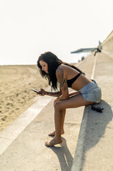 Smiling young woman with nose piercing and tattoos using smartphone near the beach - GIOF04636