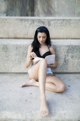 Portrait of tattooed young woman with black hair reading a book - GIOF04642