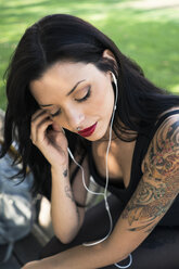 Portrait of young woman with nose piercing and tattoos listening music with earphones - GIOF04656
