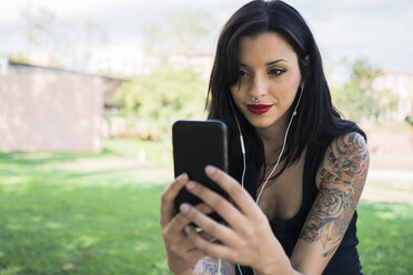 Portrait of smiling young woman with nose piercing and earphones taking selfie with smartphone - GIOF04657