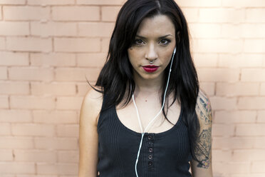 Portrait of young woman with nose piercing and tatoo using earphones - GIOF04660