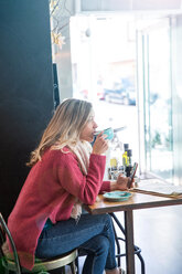 Woman sitting in cafe, drinking coffee, holding smartphone - CUF45114