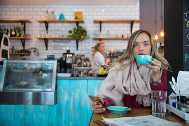 Frau sitzt in einem Café, hält ihr Smartphone und trinkt Kaffee - CUF45121