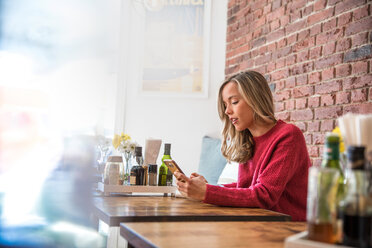 Frau sitzt im Café und schaut auf ihr Smartphone - CUF45127