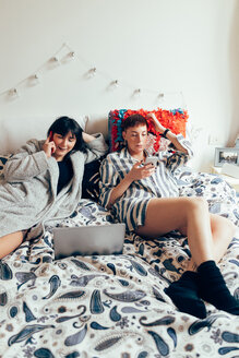 Frauen entspannen sich auf dem Bett und benutzen Laptop und Mobiltelefon - CUF45147
