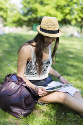 Young student sitting on a meadow in a park using digital tablet - GIOF04683