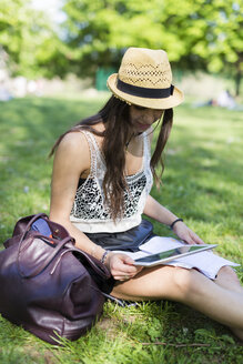 Junge Studentin sitzt auf einer Wiese in einem Park und benutzt ein digitales Tablet - GIOF04683