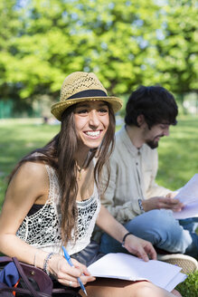 Porträt einer glücklichen jungen Studentin, die im Park sitzt - GIOF04685