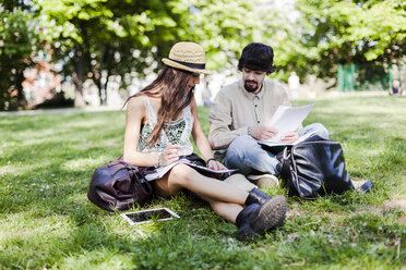 Zwei Studenten sitzen auf einer Wiese in einem Park und sehen sich Notizen an - GIOF04686