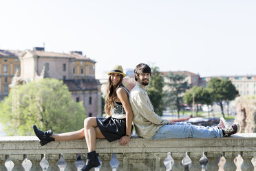 Happy young couple sitting back to back on balustrade - GIOF04697