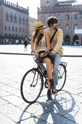 Italy, Bologna, young couple on bicycle watching something - GIOF04702