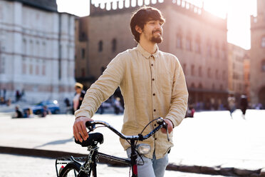 Italien, Bologna, Porträt eines entspannten jungen Mannes, der ein Fahrrad in der Stadt schiebt - GIOF04707