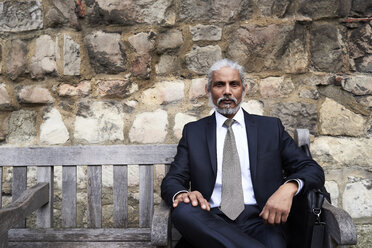 Porträt eines älteren Geschäftsmannes, der auf einer Bank sitzt und Anzug und Krawatte trägt - IGGF00610
