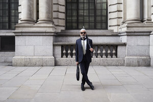 UK, London, Porträt eines eleganten Geschäftsmannes mit Sonnenbrille und Regenschirm in Anzug und Krawatte - IGGF00619