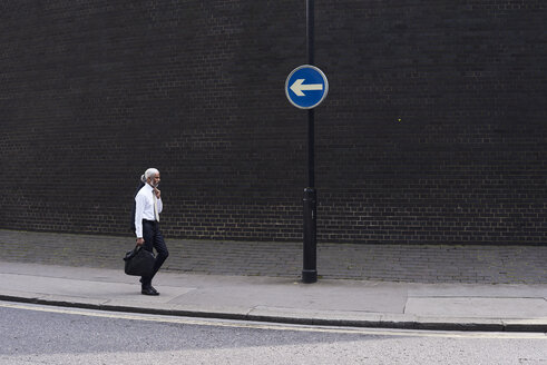 Eleganter älterer Geschäftsmann mit Gepäck, der auf dem Bürgersteig in die entgegengesetzte Richtung geht - IGGF00628