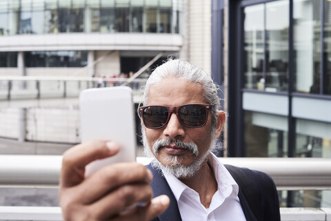 Porträt eines grauhaarigen älteren Geschäftsmannes, der ein Selfie mit seinem Smartphone macht, lizenzfreies Stockfoto