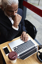 Senior businessman working on laptop in a coffee shop - IGGF00637