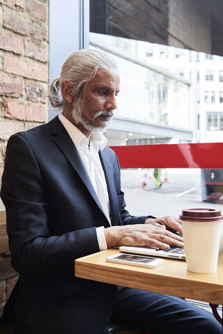 Senior businessman sitting in a coffee shop working on laptop stock photo