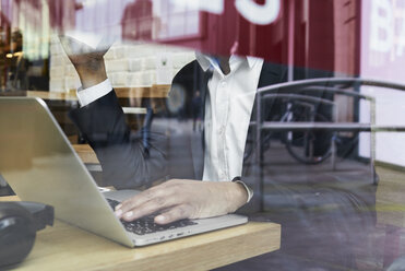 Älterer Geschäftsmann hinter einer Fensterscheibe in einem Café bei der Arbeit am Laptop - IGGF00639
