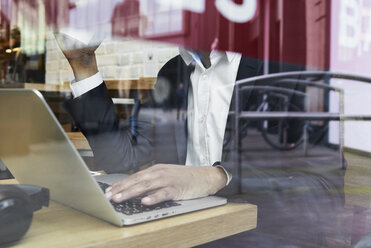 Senior businessman behind windowpane in a coffee shop working on laptop - IGGF00639