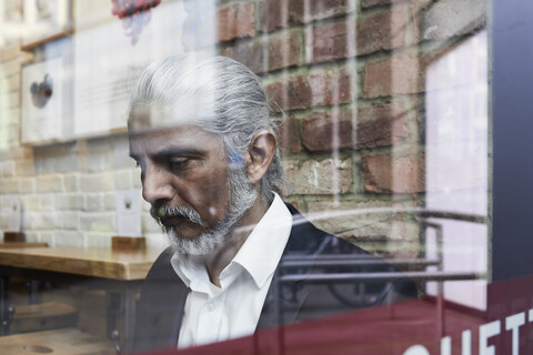 Älterer Geschäftsmann hinter einer Fensterscheibe in einem Kaffeehaus, lizenzfreies Stockfoto
