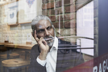 Porträt eines nachdenklichen älteren Geschäftsmannes in einem Café mit Blick aus dem Fenster - IGGF00642