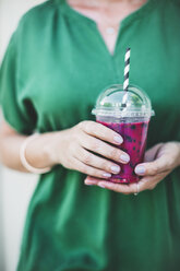 Woman's hands holding plastic cup of pink smoothie, close-up - HMEF00017