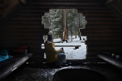 Finnland, Kuopio, Frau sitzt im Winter in Holzhütte und schaut auf Lagerfeuer, lizenzfreies Stockfoto