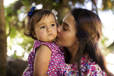 Young woman kissing serious looking baby girl - VABF01620