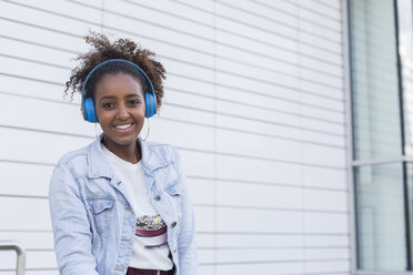 Porträt einer lächelnden jungen Frau, die mit Kopfhörern Musik hört - JUNF01481